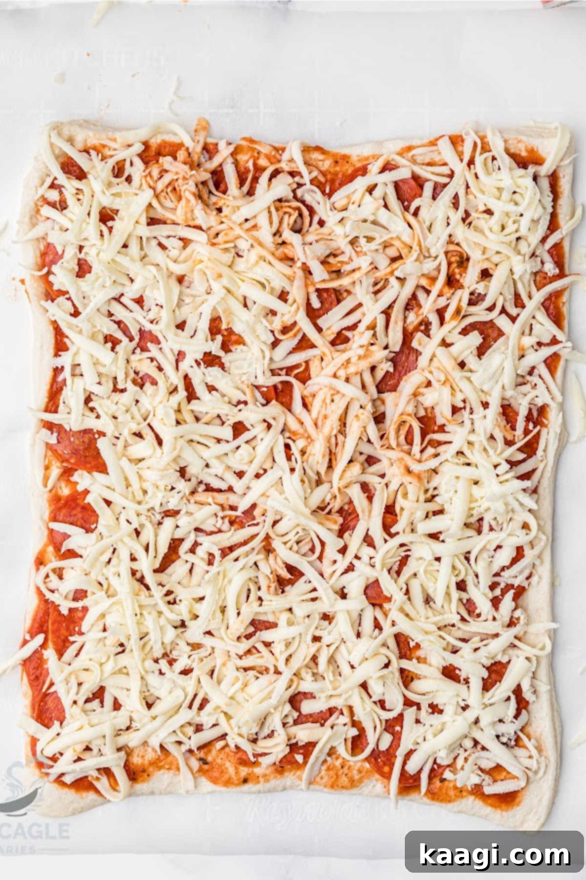 Shredded mozzarella cheese and pepperoni slices layered over pizza sauce on puff pastry.