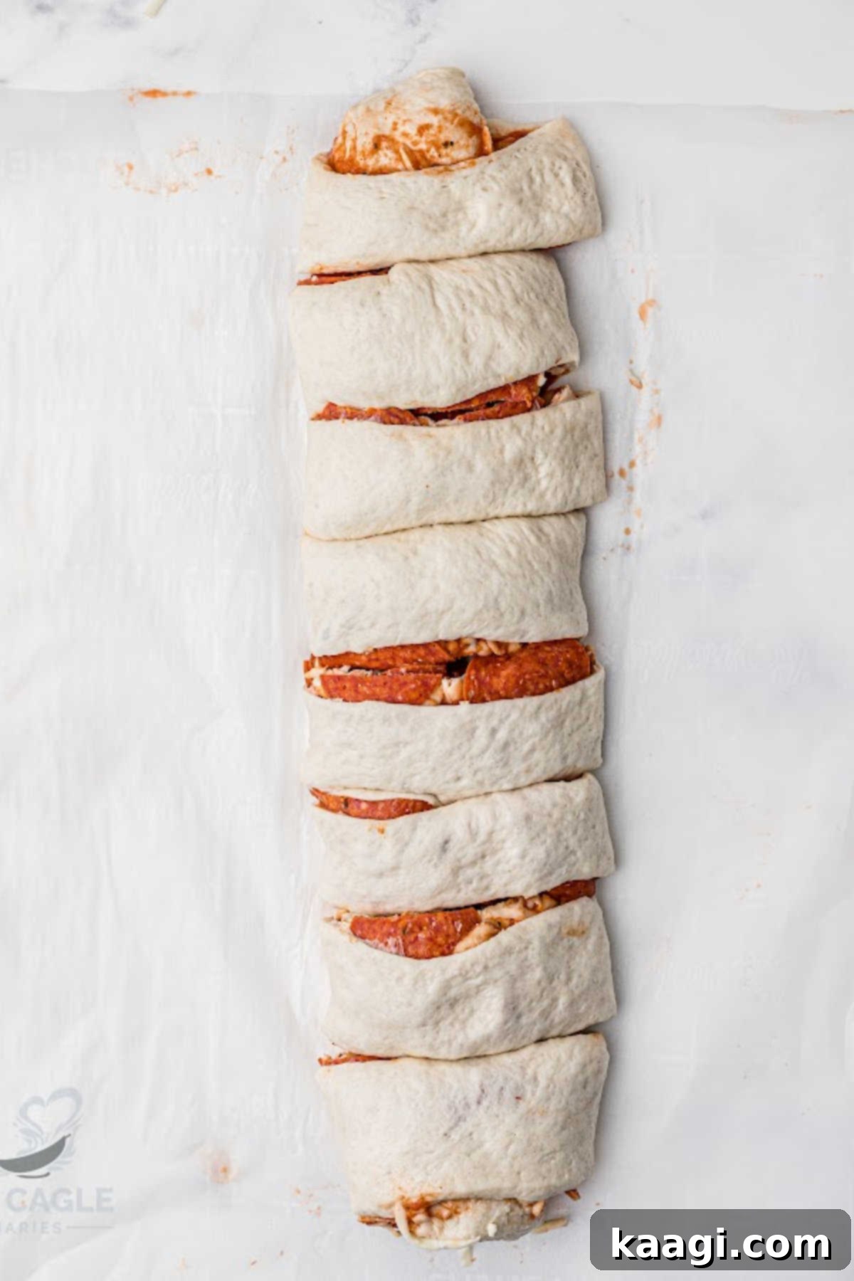 A tightly rolled puff pastry filled with pizza ingredients, ready to be sliced and baked.